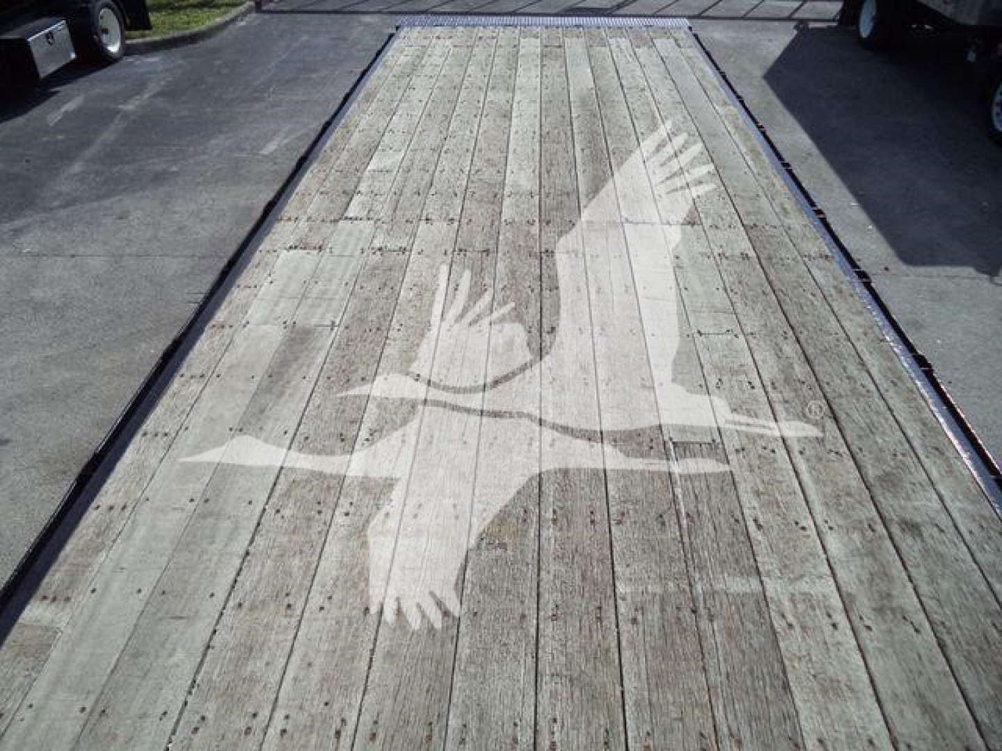 Flatbed trailer deck with a large logo of a flying crane across the wooden planks.