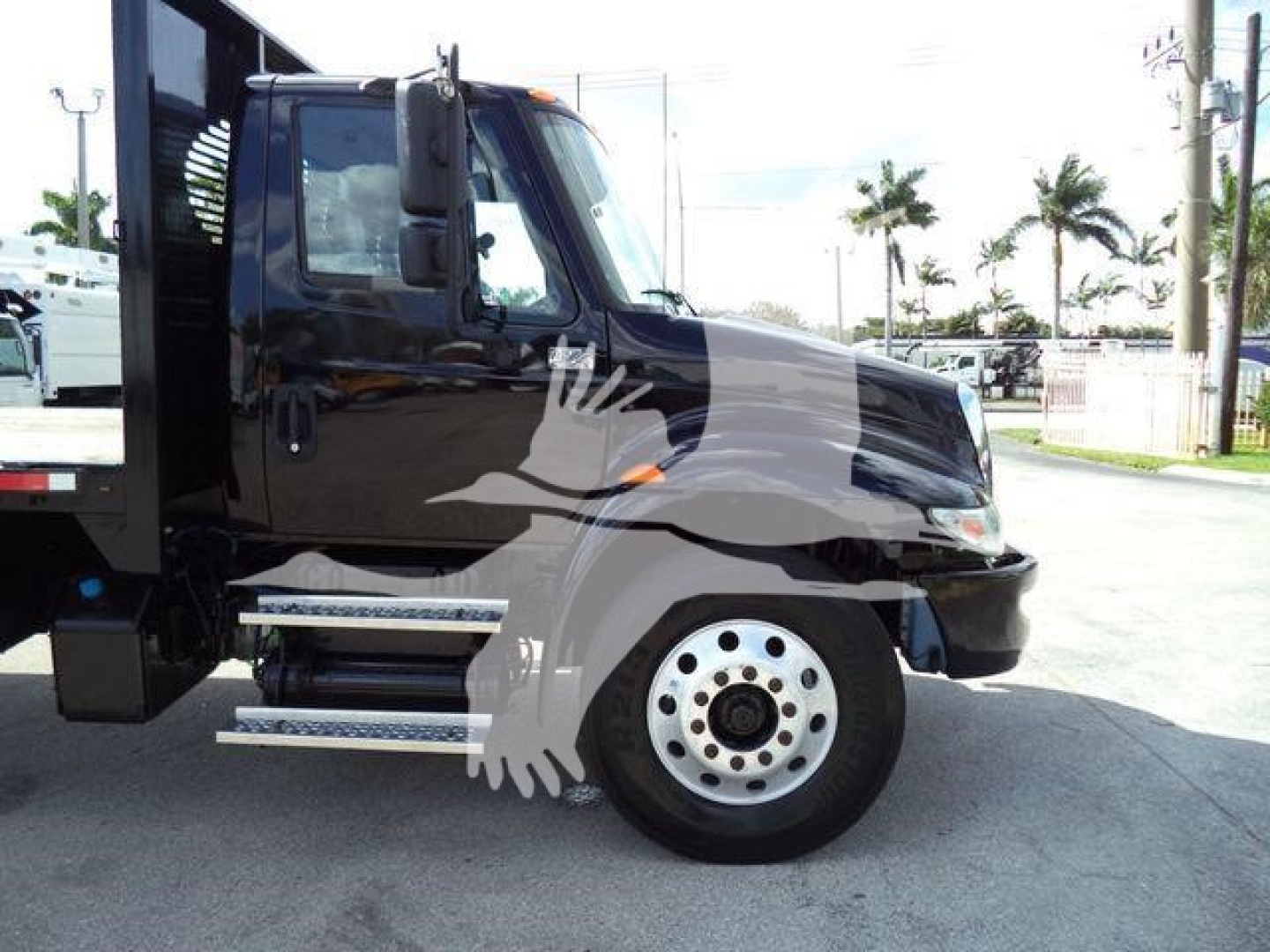 Truck cab of a 2019 International 4300 flatbed with side steps and black paint, front wheel, and partial chassis visible.