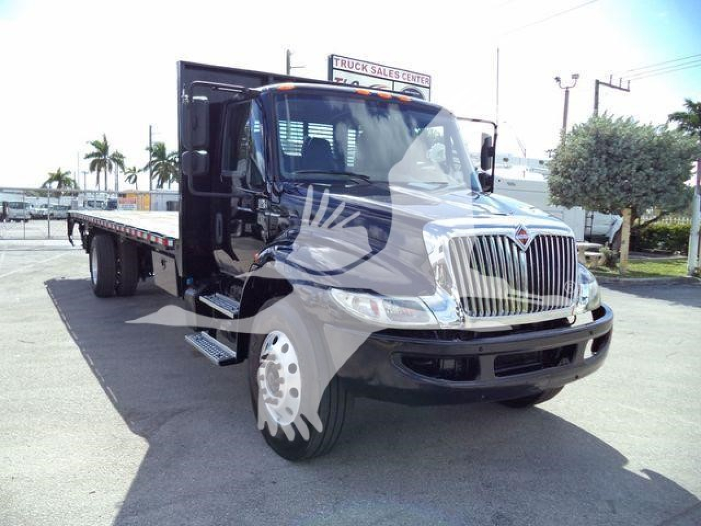 International 4300 flatbed tow truck front/right angle view with chrome grille and black cab, side steps visible.