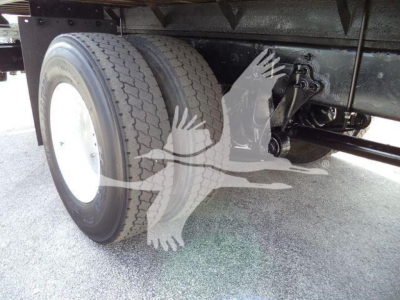Truck rear undercarriage showing dual rear wheels and suspension components of a flatbed truck.