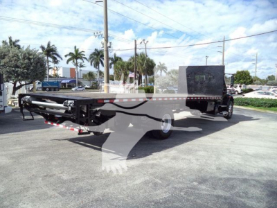 Flatbed tow truck from rear-left angle with extended platform and toolbox, black frame, and white cab in background.