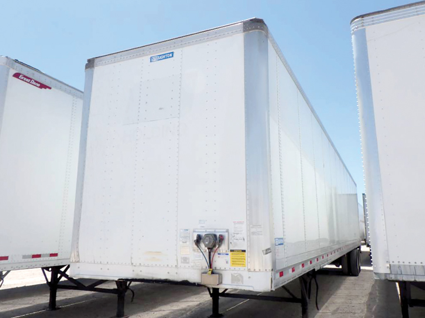 Trailer rear view showing a silver enclosed cargo trailer with Stoughton branding on door area and a visible underside support and hitch.