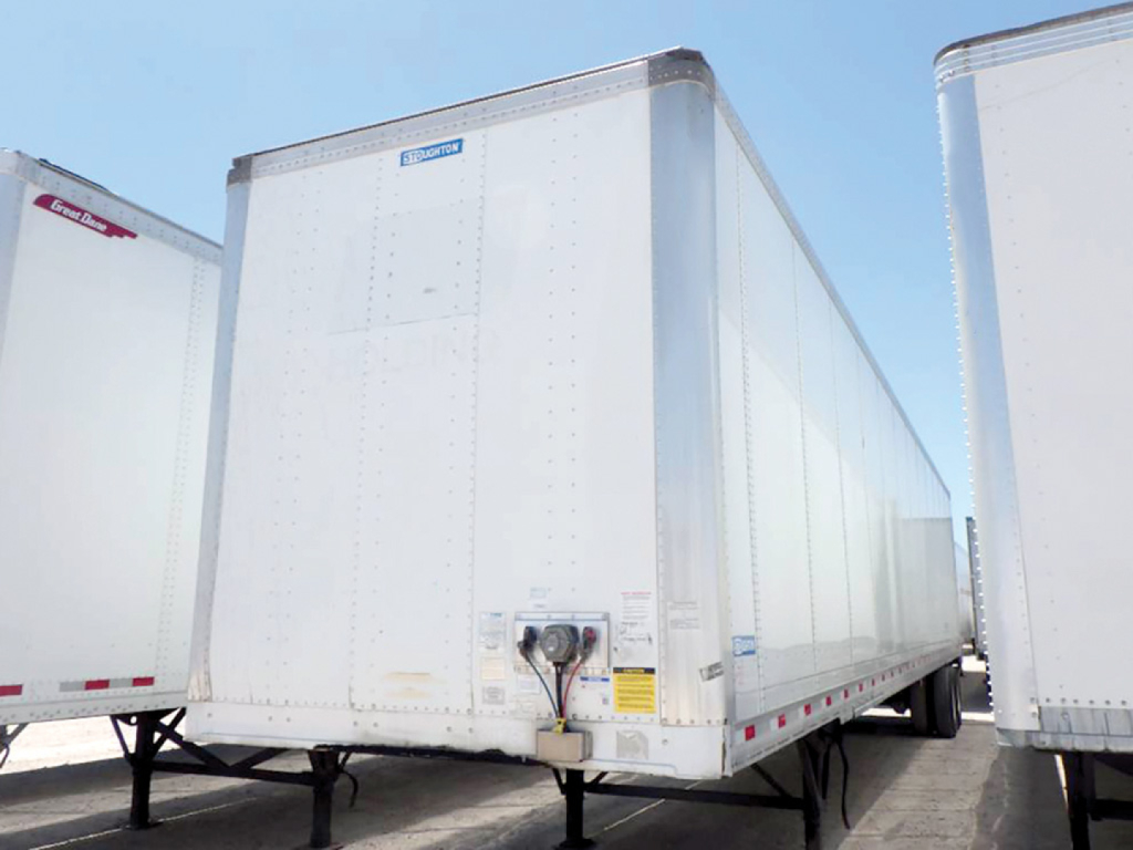Trailer rear view showing a silver enclosed cargo trailer with Stoughton branding on door area and a visible underside support and hitch.