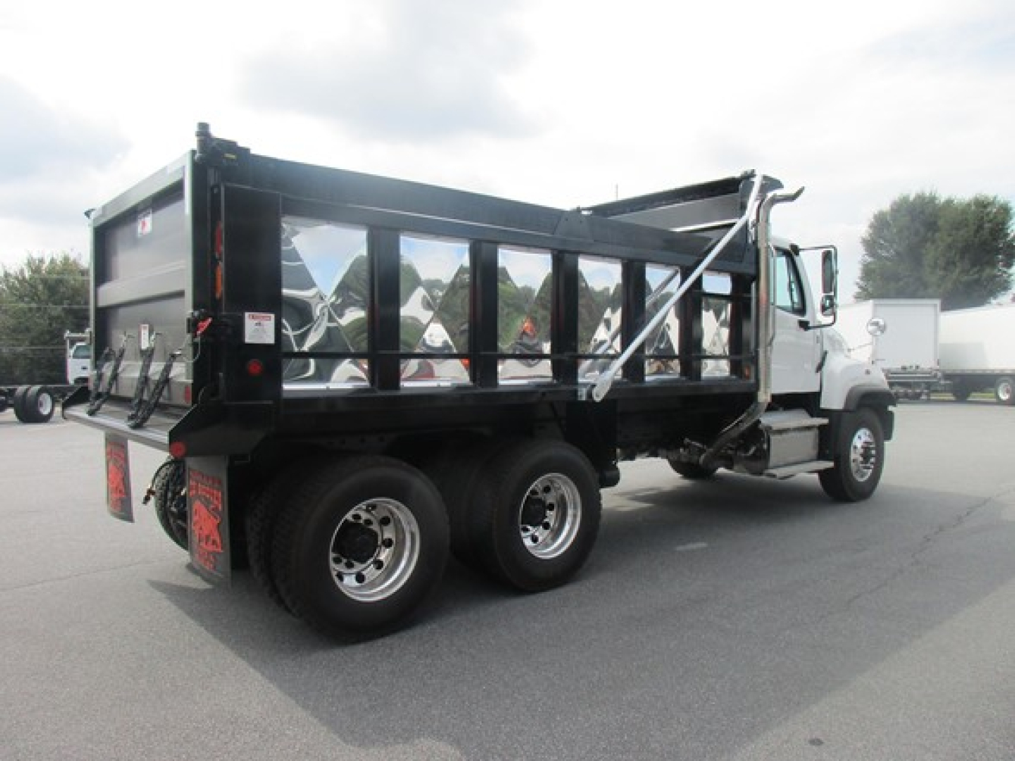 Freightliner 114SD dump truck in a dealership lot, aluminum dump body with side rails, rear view shows dual rear axles and taillights.