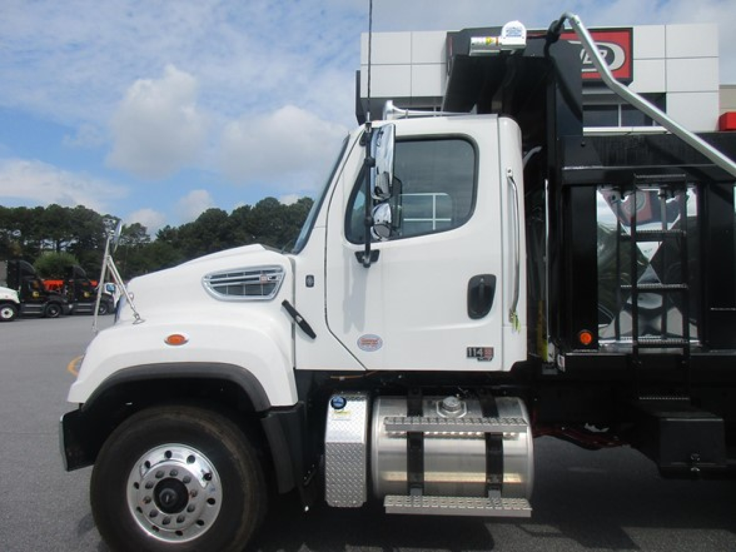 Freightliner 114SD dump truck side view showing cab and fuel tanks; white cab, chrome fuel tanks, black dump bed framework.