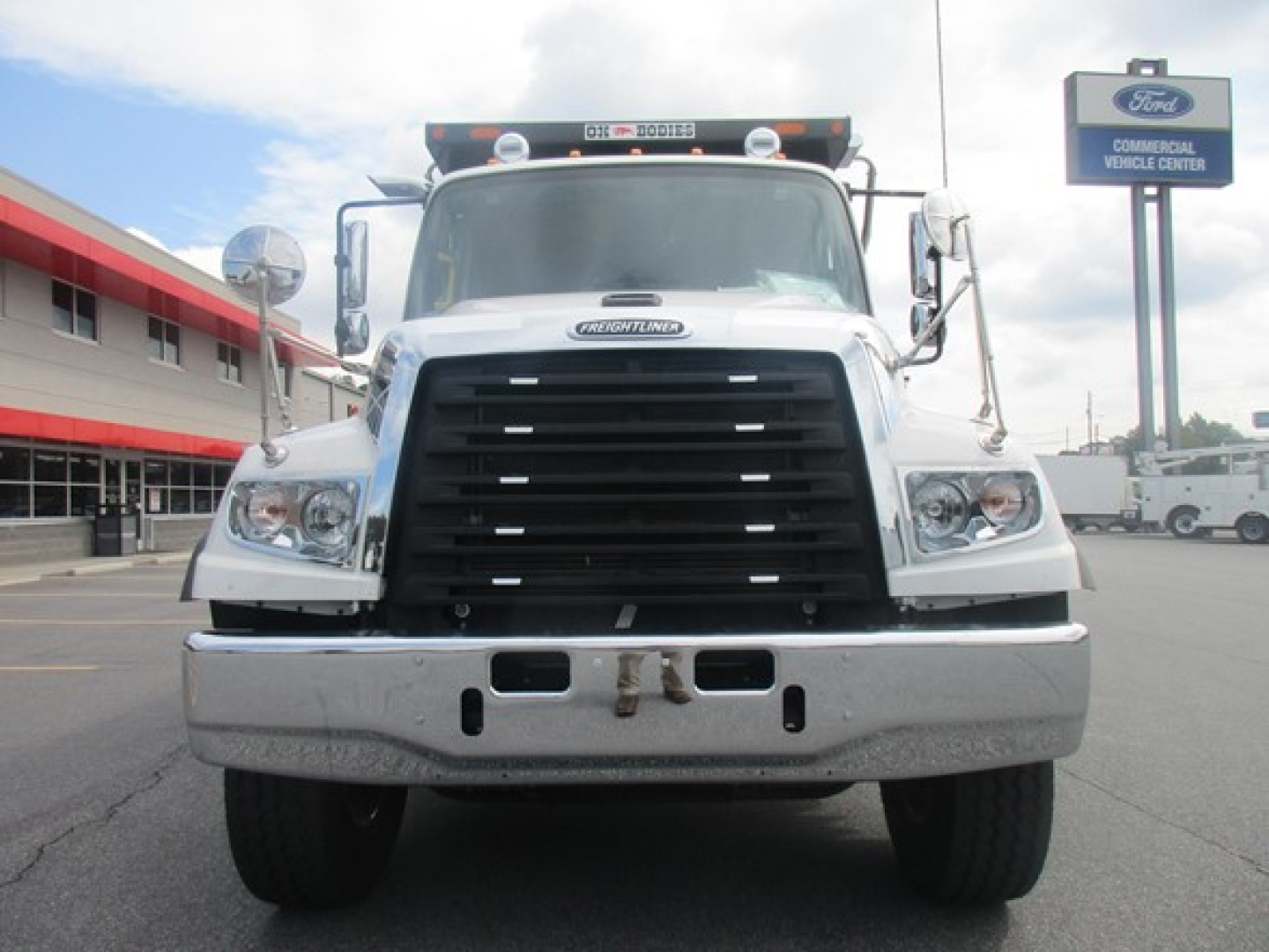 Front view of a new Freightliner 114SD dump truck showing large black grille, dual headlights, chrome bumper, and inspection mirrors.