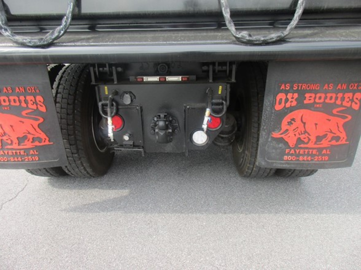 Freightliner 114SD truck rear showing towing hitch, air and electrical connections, and mud flaps with red graphics; undercarriage components visible.