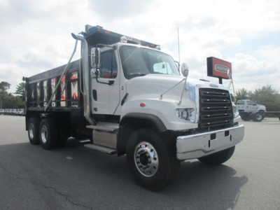Freightliner 114SD dump truck in showroom light, white cab with black dump bed, front chrome bumper, heavy-duty wheels, side steps, and cargo bed visible.