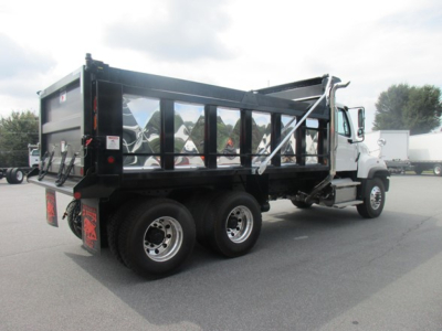 Freightliner 114SD dump truck in a dealership lot, aluminum dump body with side rails, rear view shows dual rear axles and taillights.
