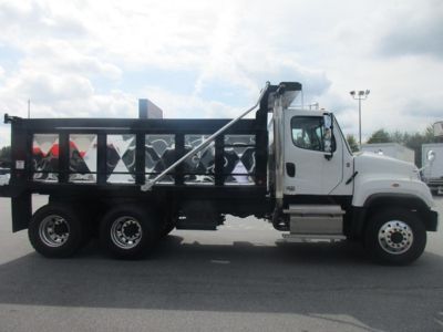 Dump truck side view showing Freightliner 114SD with black dump bed, white cab, and side crane raised.
