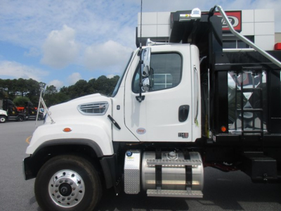 Freightliner 114SD dump truck side view showing cab and fuel tanks; white cab, chrome fuel tanks, black dump bed framework.