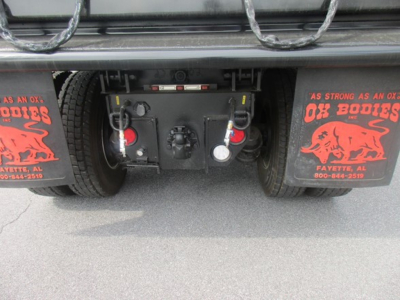 Freightliner 114SD truck rear showing towing hitch, air and electrical connections, and mud flaps with red graphics; undercarriage components visible.