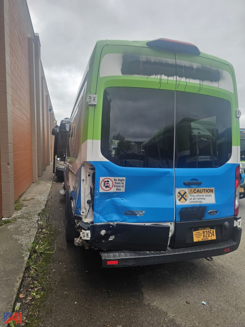Rear view of a 2019 Ford Transit full-size van in green and blue with damaged rear bumper and caution stickers.