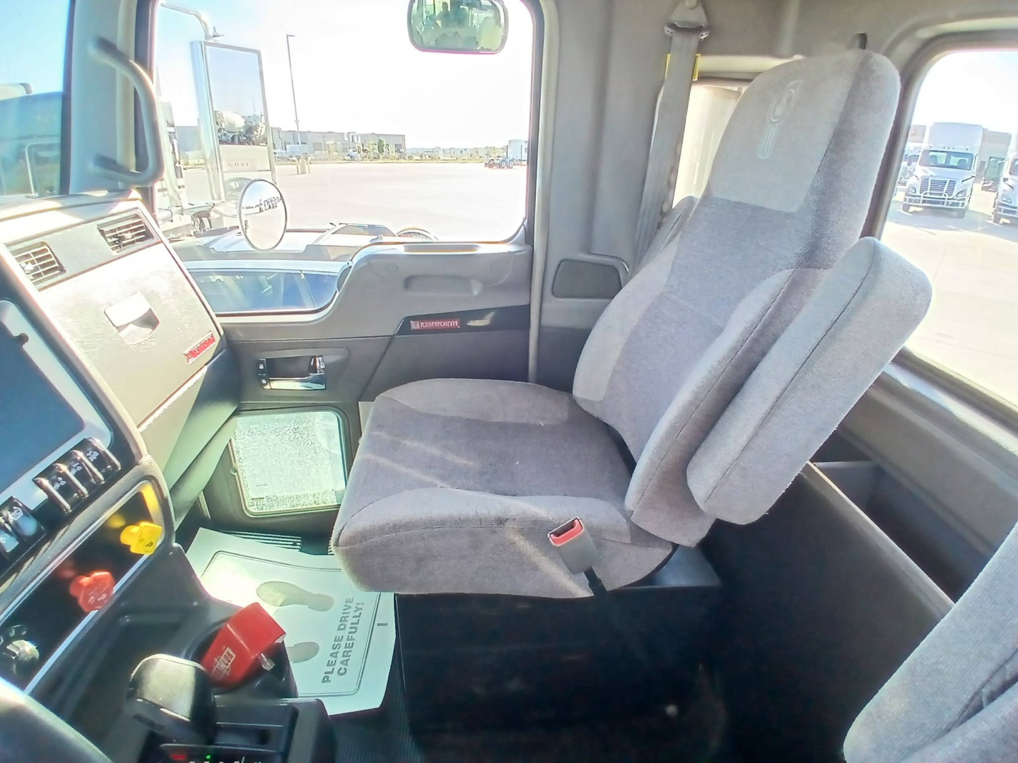 Kenworth T800 truck dashboard and front seats in cabin, gray fabric seats, steering area, visor and window view with other trucks outside.