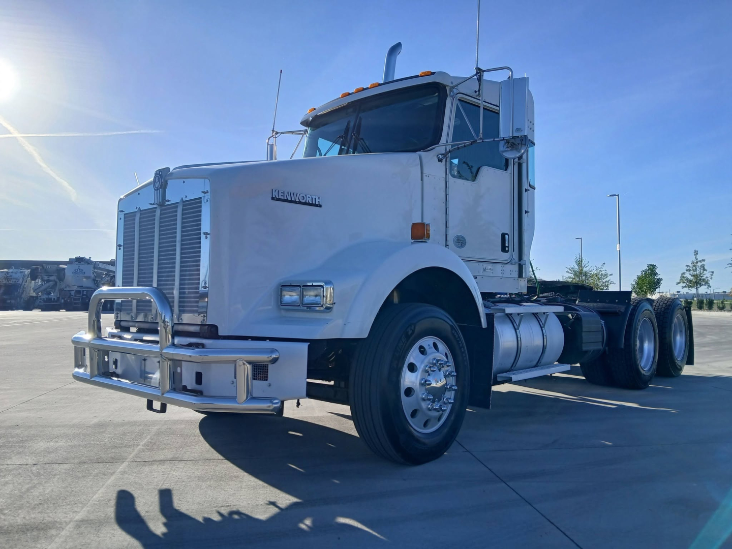 Kenworth T800 conventional sleeper truck in a parking lot showing front grille, bumper guard, and dual rear axles.
