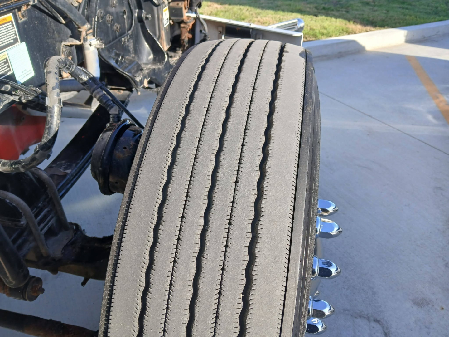 Kenworth truck front wheel area showing tire and suspension components with VIN/stock info in background. No explicit text readable beyond vehicle context.