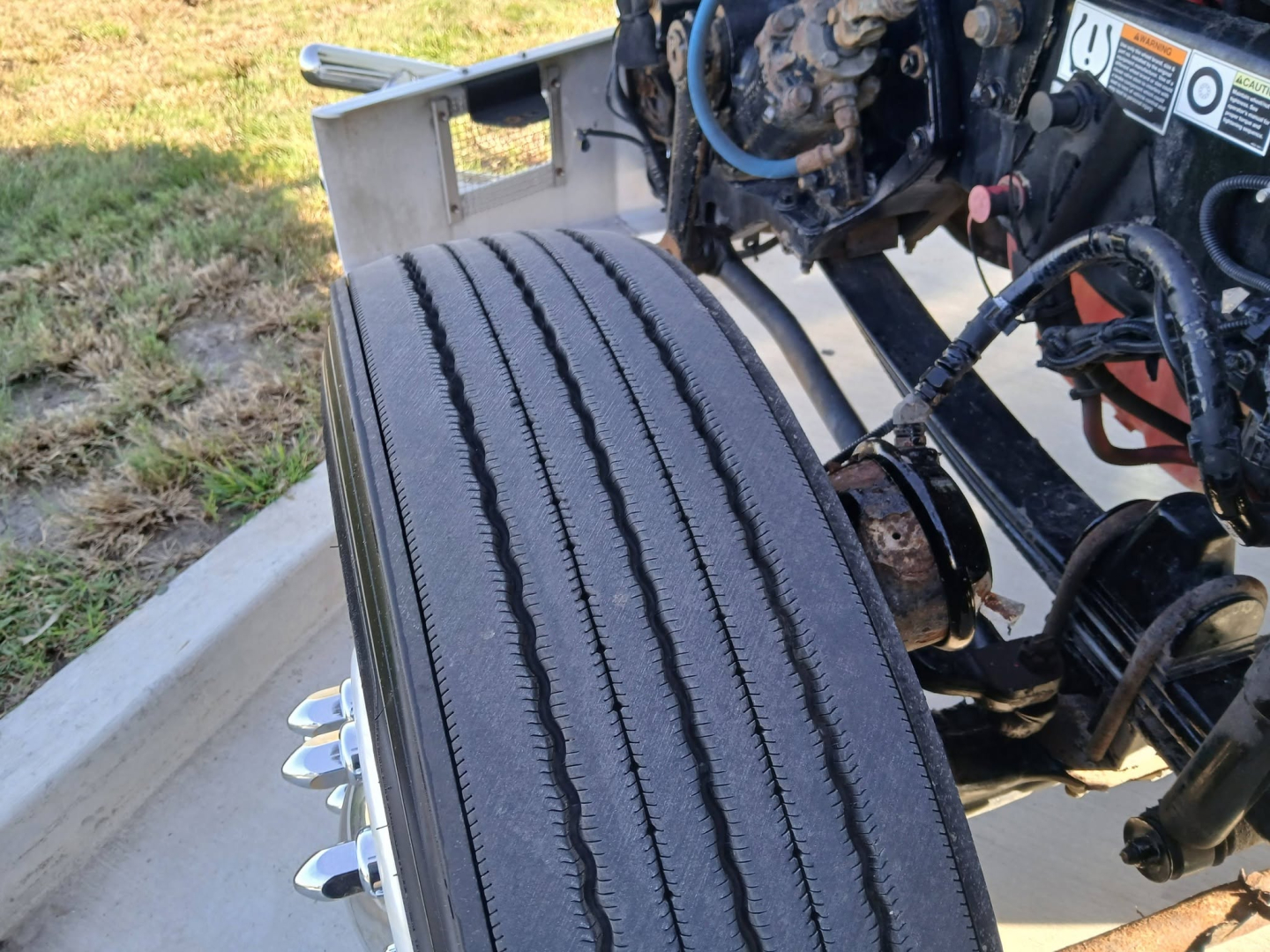 Kenworth T800 truck front wheel and undercab components visible, partial engine bay, hydraulic lines, and suspension mounting.