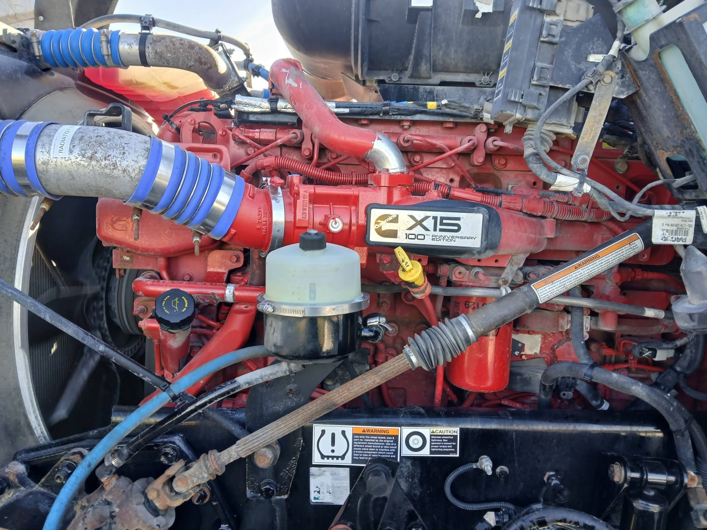 Kenworth T800 engine bay showing X15 label on red engine with blue hoses and yellow dipstick cap.