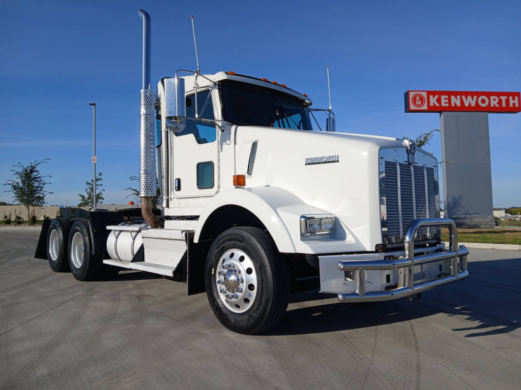 Kenworth T800 truck in a dealership lot, white cab with chrome bumper and exhaust stacks, Kenworth sign in background.