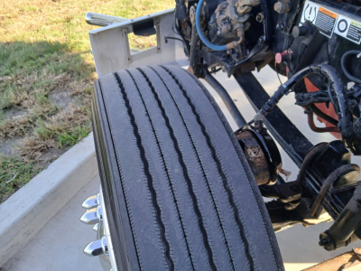 Kenworth T800 truck front wheel and undercab components visible, partial engine bay, hydraulic lines, and suspension mounting.