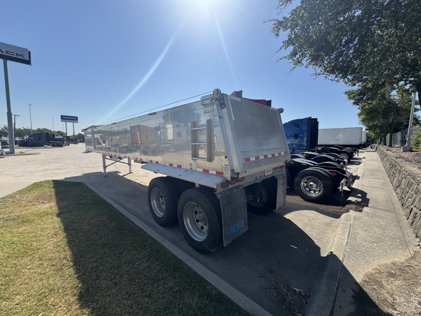 Dump trailer with polished metal sides showing tandem axle and rear dump bed.