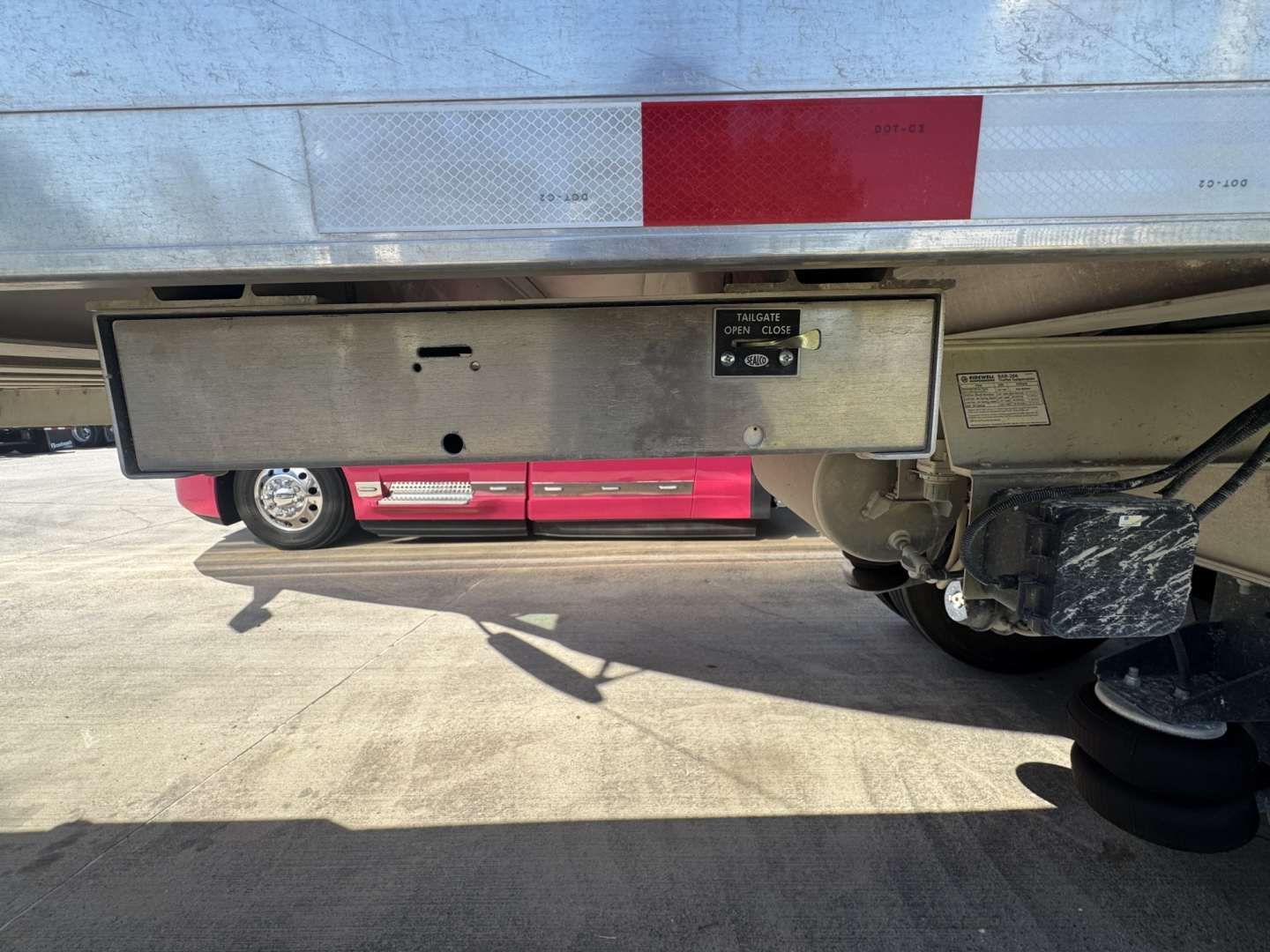 Trailer undercarriage showing storage box and rear axle with hydraulic components and landing gear; text on box not legible.