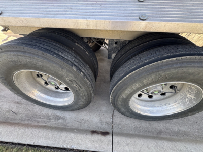 Dual rear trailer wheels and a portion of the aluminum deck showing two tires and rims under a dump trailer.