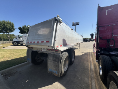 Dump trailer showing rear and side panels with reflective red/white tape, dual rear wheels, and mudflaps; Hicks SL3932 trailer branding faint on side.