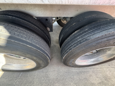 Rear dual axles with four tires on a dump trailer; close-up of wheel rims and tires under the trailer bed; no readable text visible.