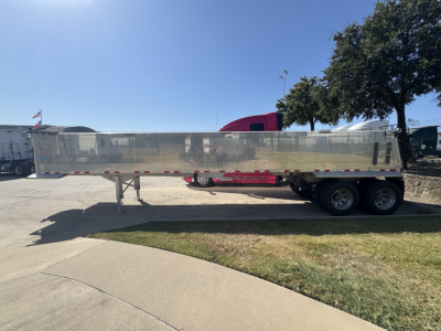 Dump trailer showing side profile of metal dump trailer with dual rear axles and reflective striping.