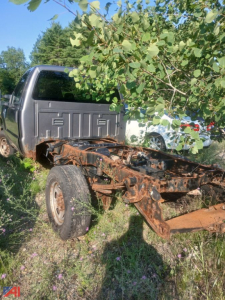 Ford F-250 cab and chassis frame with rust and exposed suspension showing in an overgrown lot.