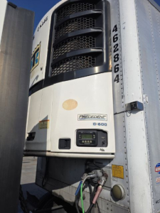 Front of an Ingersoll Rand or similar Reefer trailer refrigeration unit on a 2005 Utility 3000R, with cooling condenser grill, model label, control panel, and connection hoses visible.