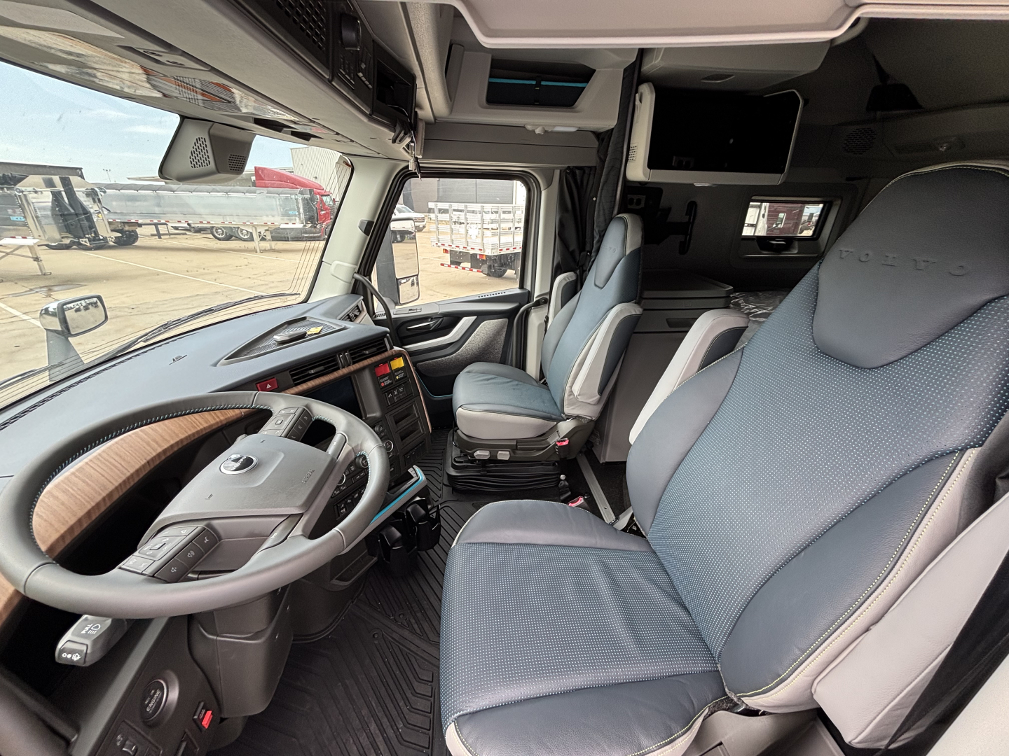 Volvo VNL cabin interior showing steering wheel, dashboard with control panel, driver seat, passenger seat, and overhead storage near windshield.