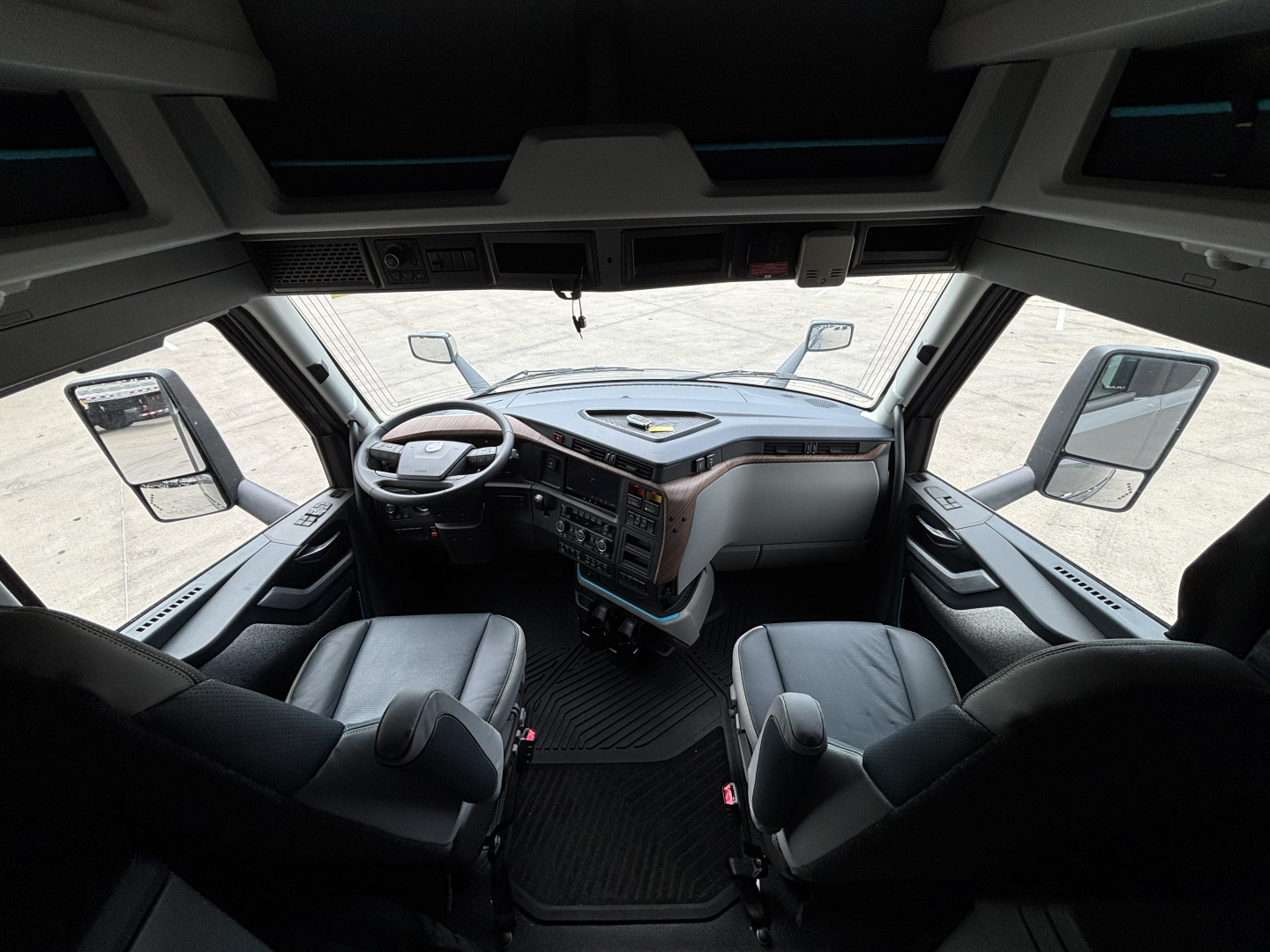 Volvo VNL64T860 truck cabin dashboard with steering wheel, two front seats, large windshield, and mirrors visible.