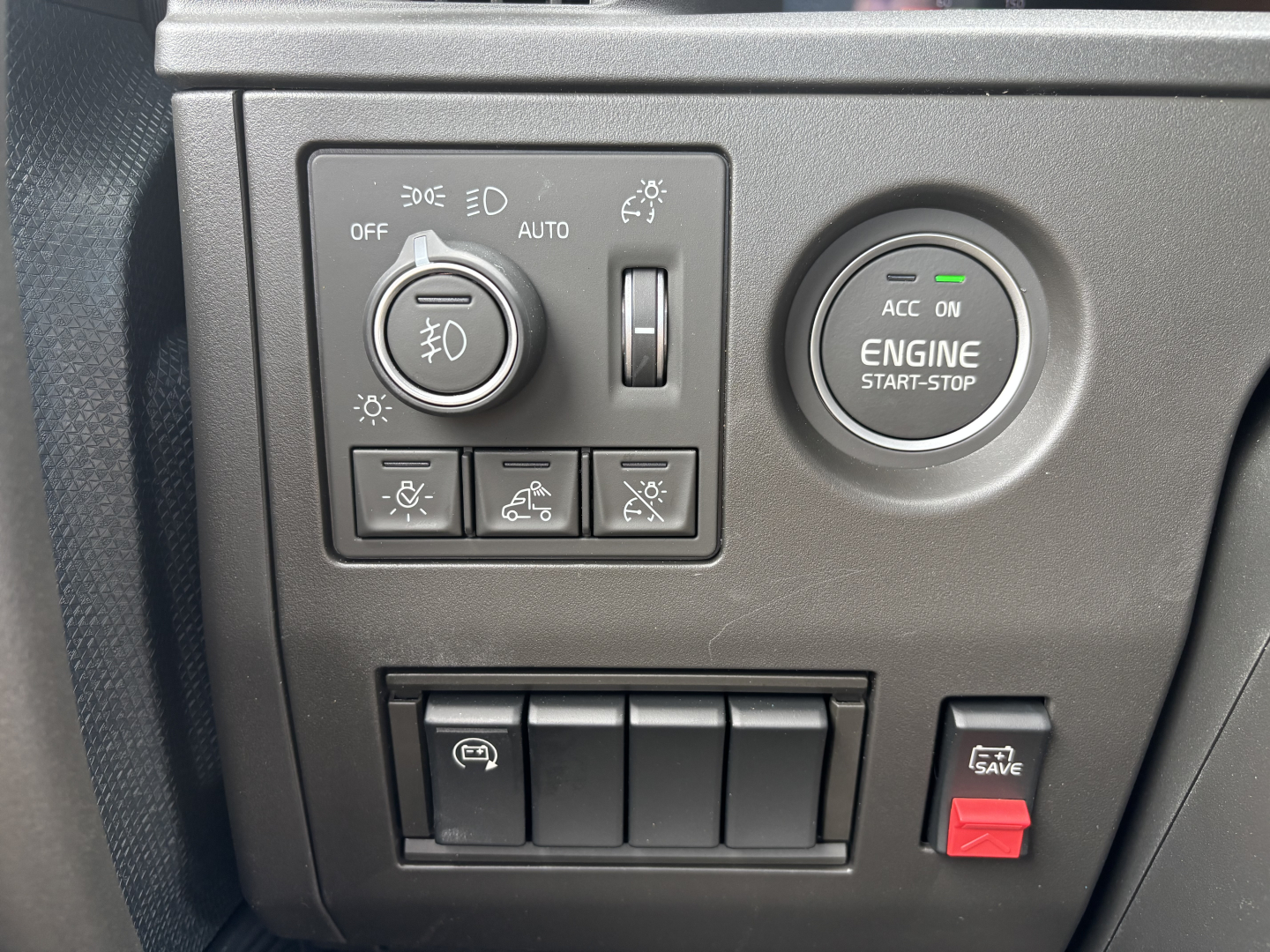Volvo engine bay area controls panel showing headlight dial, engine start-stop button, and several auxiliary switches in a new Volvo VNL64T860 interior.