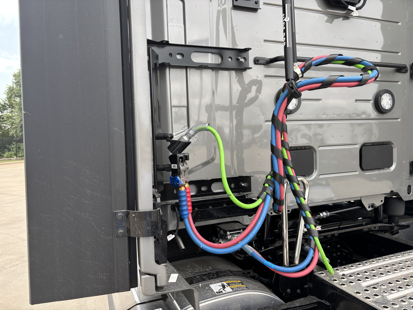 Volvo VNL64T860 truck rear view showing colorful braided air lines, fuel/air hoses and a metal platform; corner of sleeper tractor with cables and connectors.