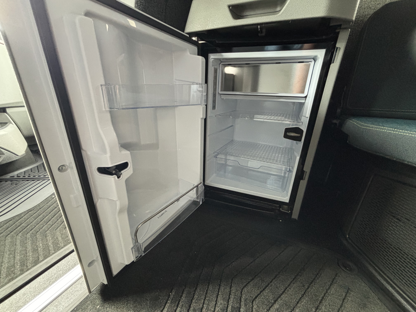 Open refrigerator/freezer unit inside a Volvo VNL64T860 truck cab showing empty shelves and door compartments.
