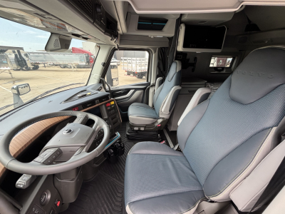 Volvo VNL cabin interior showing steering wheel, dashboard with control panel, driver seat, passenger seat, and overhead storage near windshield.