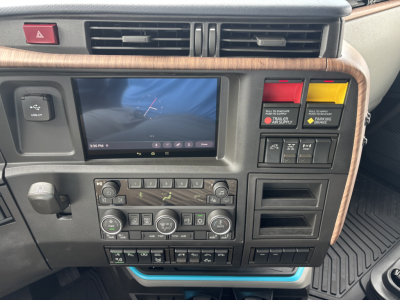 Dashboard of a Volvo truck cab showing touchscreen display, climate controls, and warning switch panels in a wooden trim bezel.
