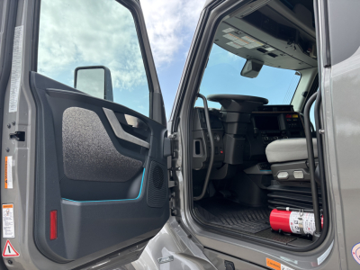 Volvo VNL64T860 cab interior and open door showing dashboard and steering wheel with a red fire extinguisher on the floor.