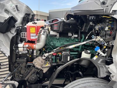 Volvo VNL64T860 engine bay showing green engine block, hoses, and coolant reservoir with blue cap; red transmission cooler reservoir and exposed components.