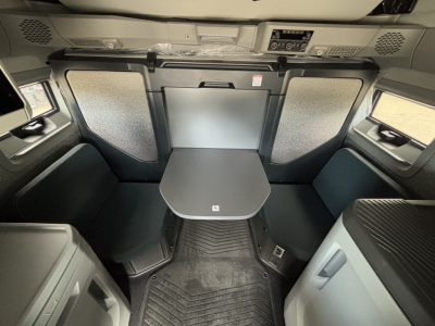 Truck cab interior showing sleeper area with table and seating; overhead control panel and window side panels visible.