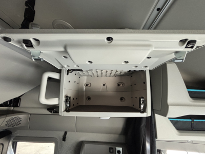 Volvo VNL-64T860 cab interior showing open overhead storage compartment with white interior and latching handles, dash area below, and seats visible.