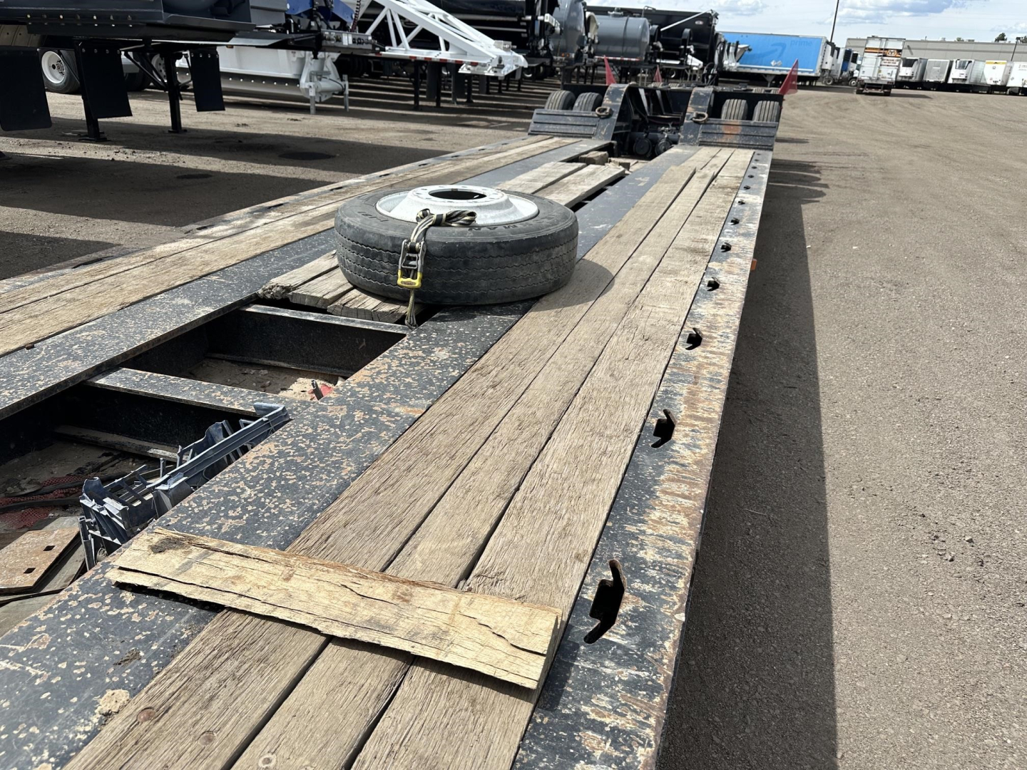 Trailer deck of a Load King lowboy with wooden decking, spare tire, and metal frame visible