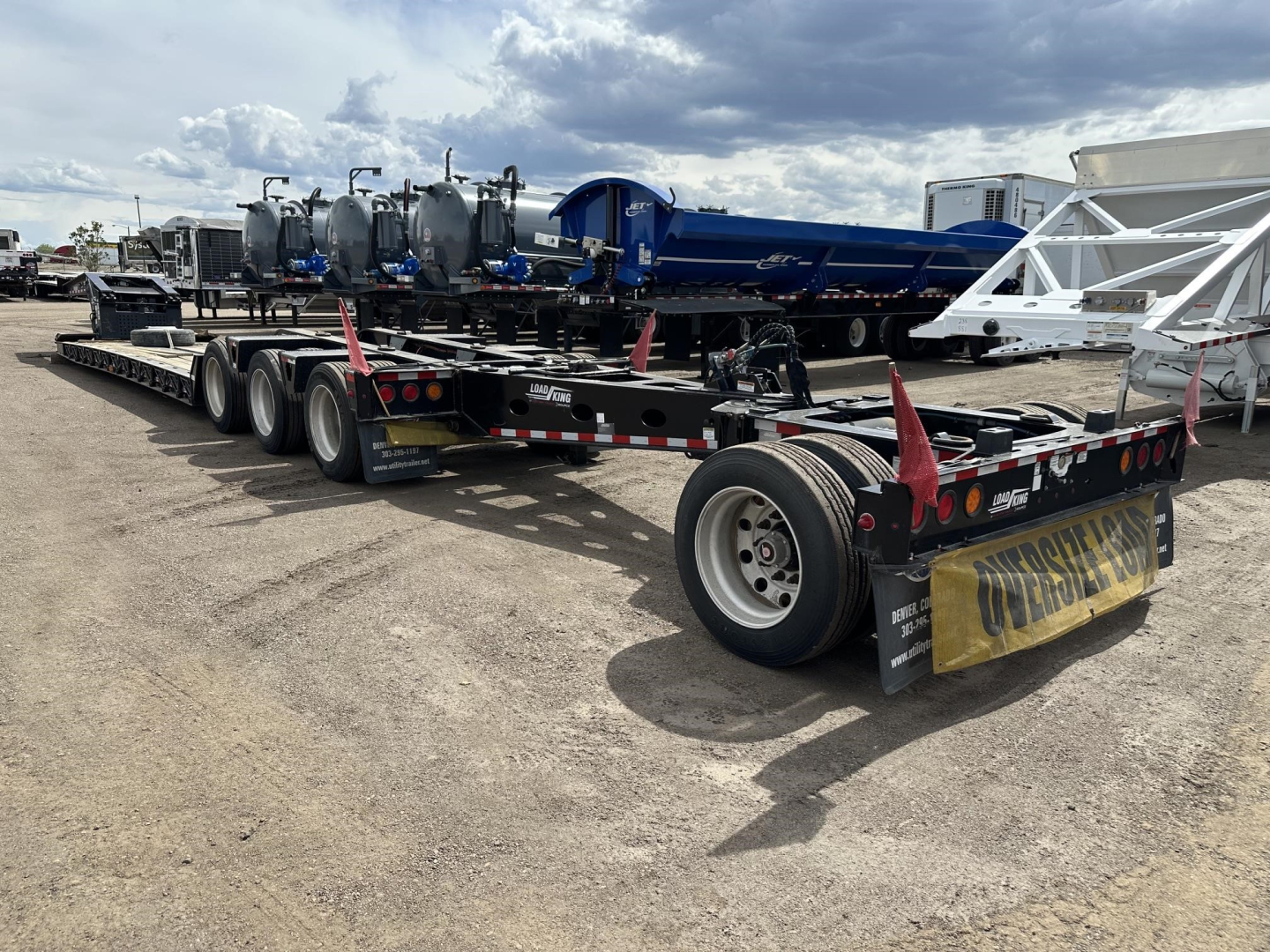 Load King lowboy trailer with multiple axles and equipment pieces loaded, rear view showing tires, ramps, and reflective tape.