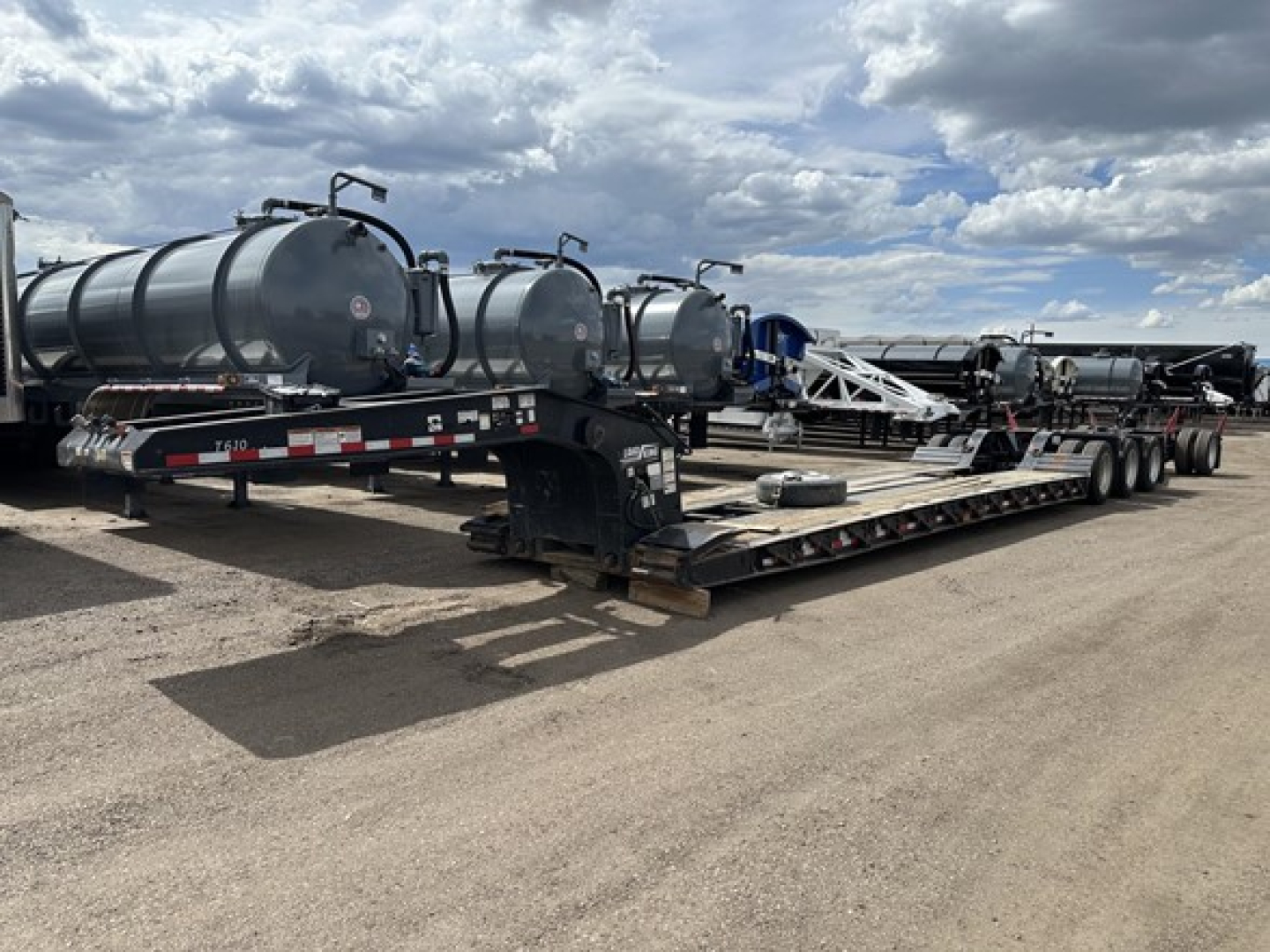 Trailer with multiple cylindrical tanks on a long lowboy chassis showing hydraulic ramps and tanker attachments.