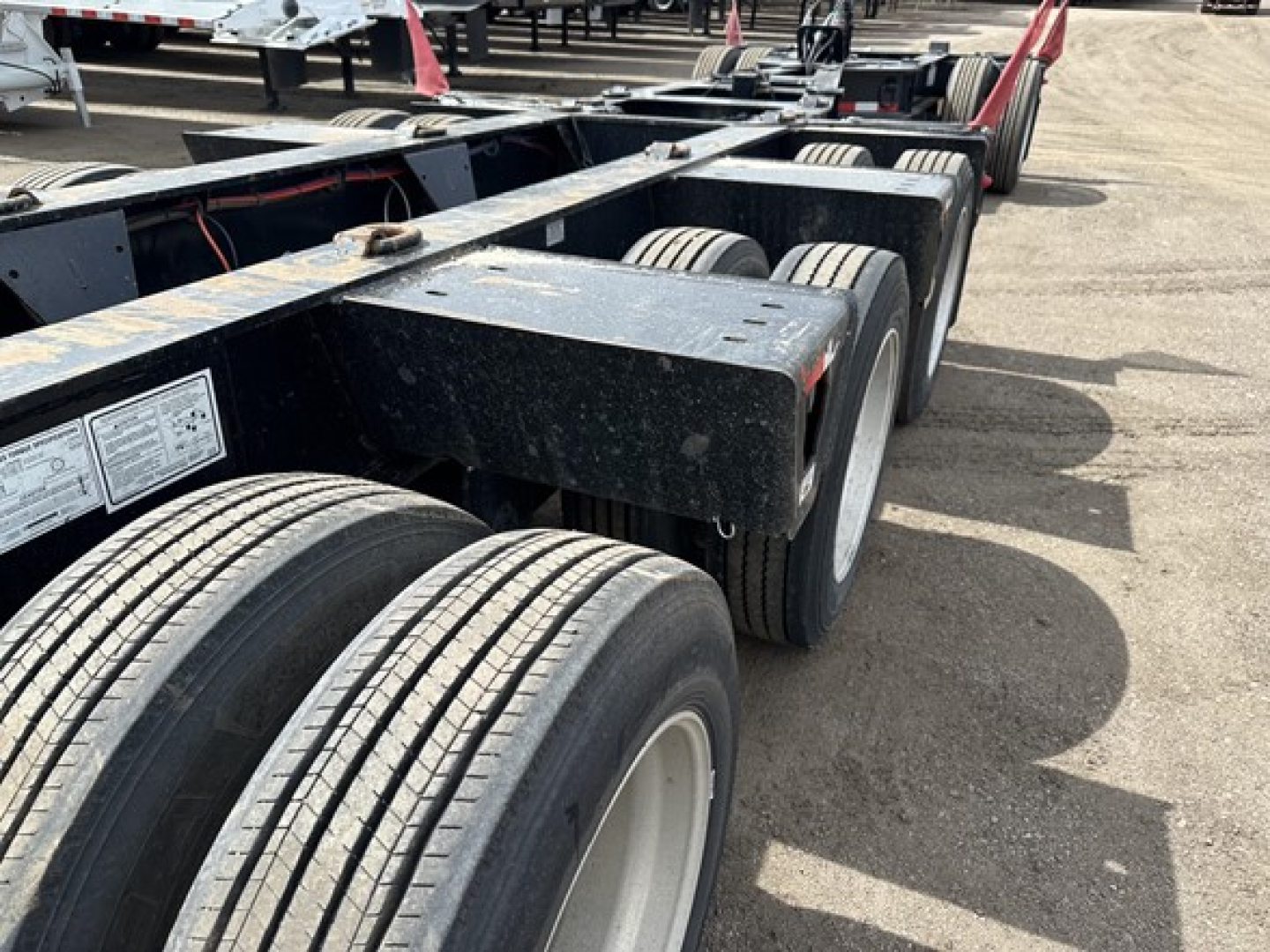 Trailer chassis with multiple axles and heavy-duty tires for Load King Mech Stinger, showing black steel frame and white wheel rims.