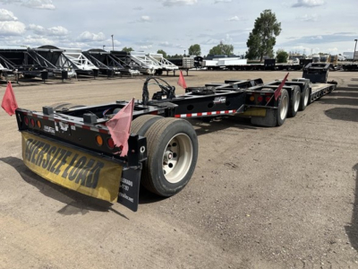 Load King Mech Stinger lowboy trailer showing multi-axle configuration with rear mudflaps and reflective tape, yellow tail tarp, and pink corner flags visible in a storage yard.