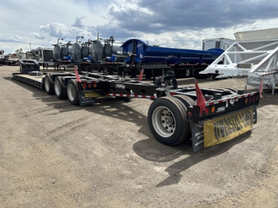 Load King mech stinger lowboy trailer with multiple axles and blue equipment on deck, rear view showing tags and tires.