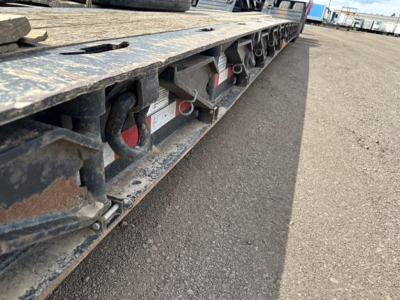 Flatbed trailer side view showing link-style hinges and red reflectors along the underside of a Load King Mech Stinger trailer edge.